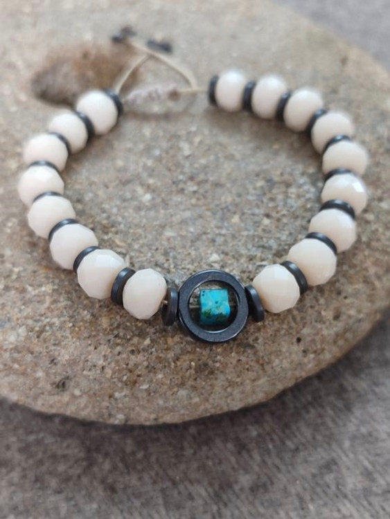 این دستبند با مرکزیت حلقه حدید و مکعب فیروزه، نمادی از قدرت درونی، محافظت و آرامش ذهنی است. دورتادور دستبند با اونیکس سفید تکمیل شده که انرژیهای مثبت را جذب و پراکندگی انرژی منفی را کاهش میدهد.